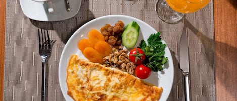 A breakfast plate with an omelette, fruits, and vegetables, a cup of coffee, and a glass of orange juice on a table.