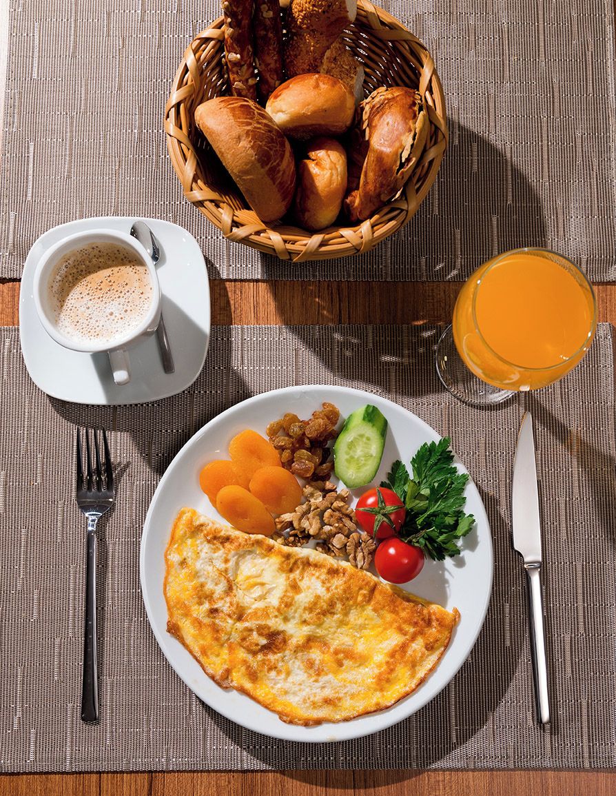 A breakfast setting with a plate of food, a basket of bread, a cup of coffee, and a glass of orange juice.