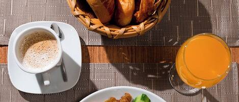 A breakfast setting with a plate of food, a basket of bread, a cup of coffee, and a glass of orange juice.