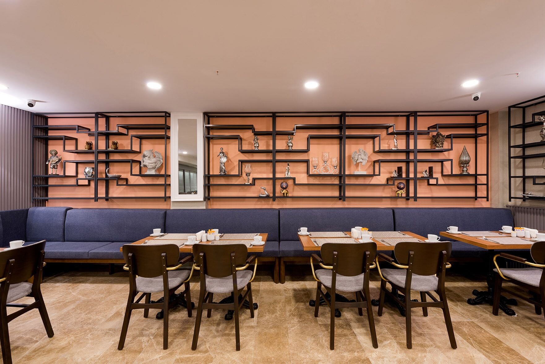 A restaurant with a long blue sofa and multiple tables with chairs.