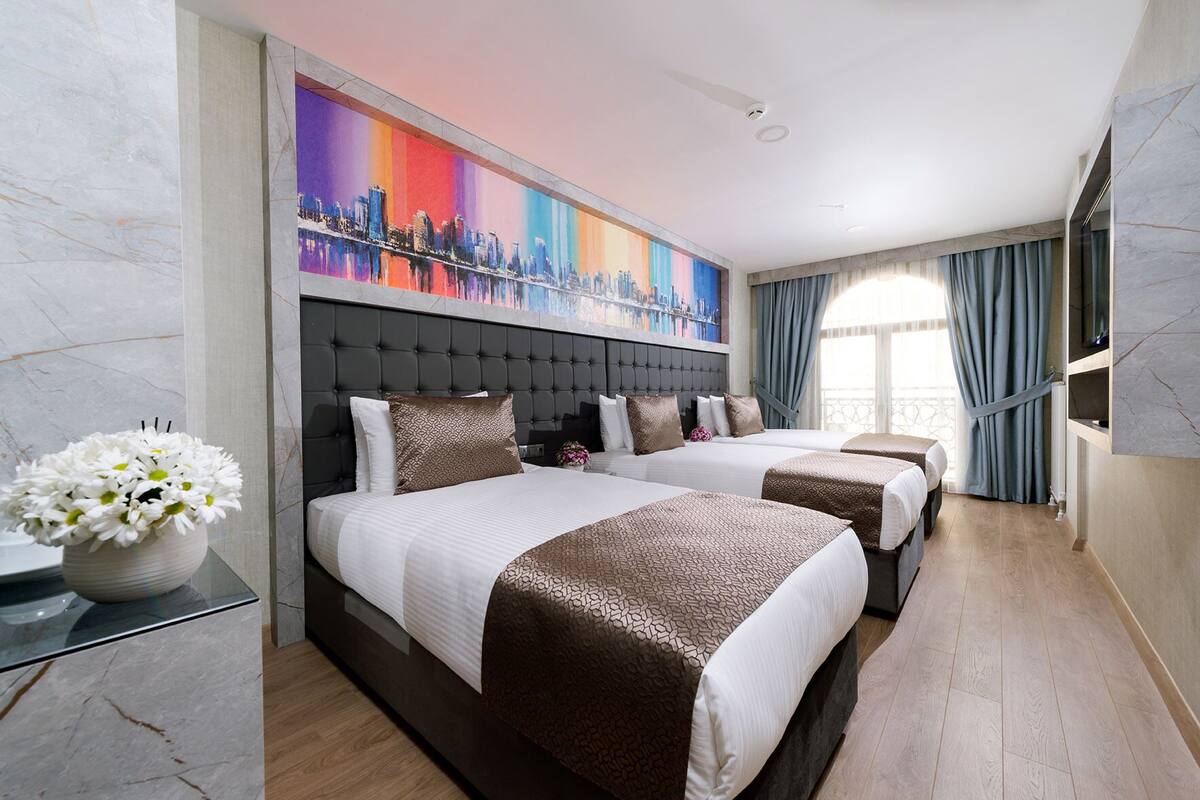 Quarto de hotel com duas camas, um mural da paisagem urbana, um vaso de flores e piso de mármore.