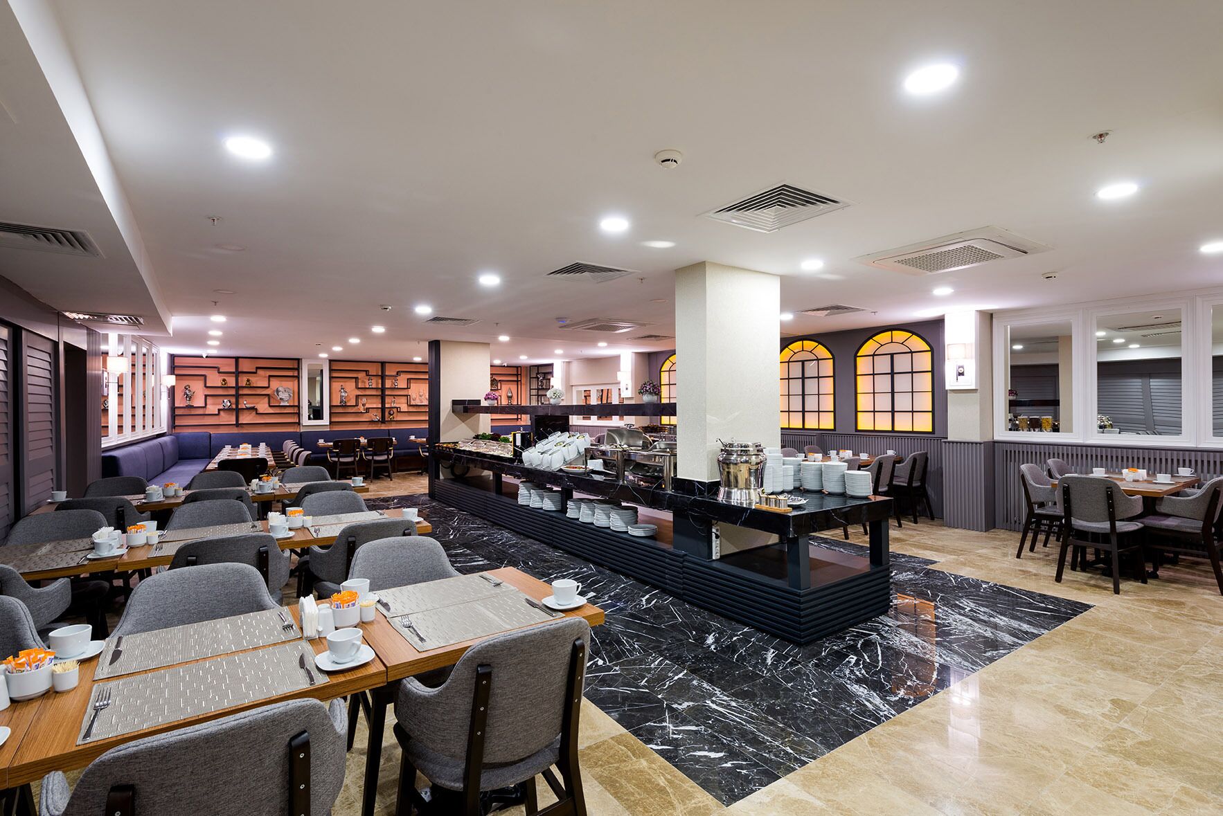 A modern restaurant with multiple dining areas, a buffet station, and a seating area with a sofa.