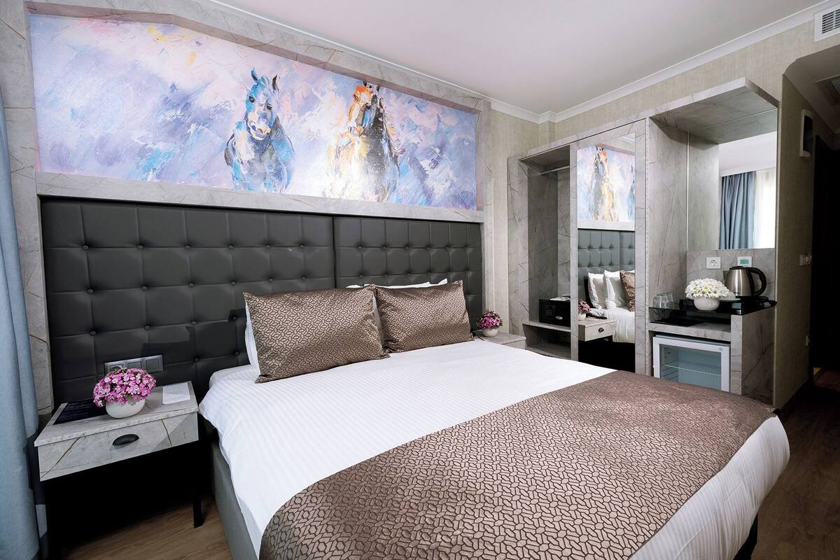 Quarto de hotel moderno com uma cama grande, cabeceira estofada cinza, parede de mármore e uma grande pintura abstrata acima da cama.