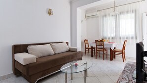 A living room with a brown sofa, a glass coffee table, and a dining area with a table and chairs. - Tihi Val Apartments (Split)