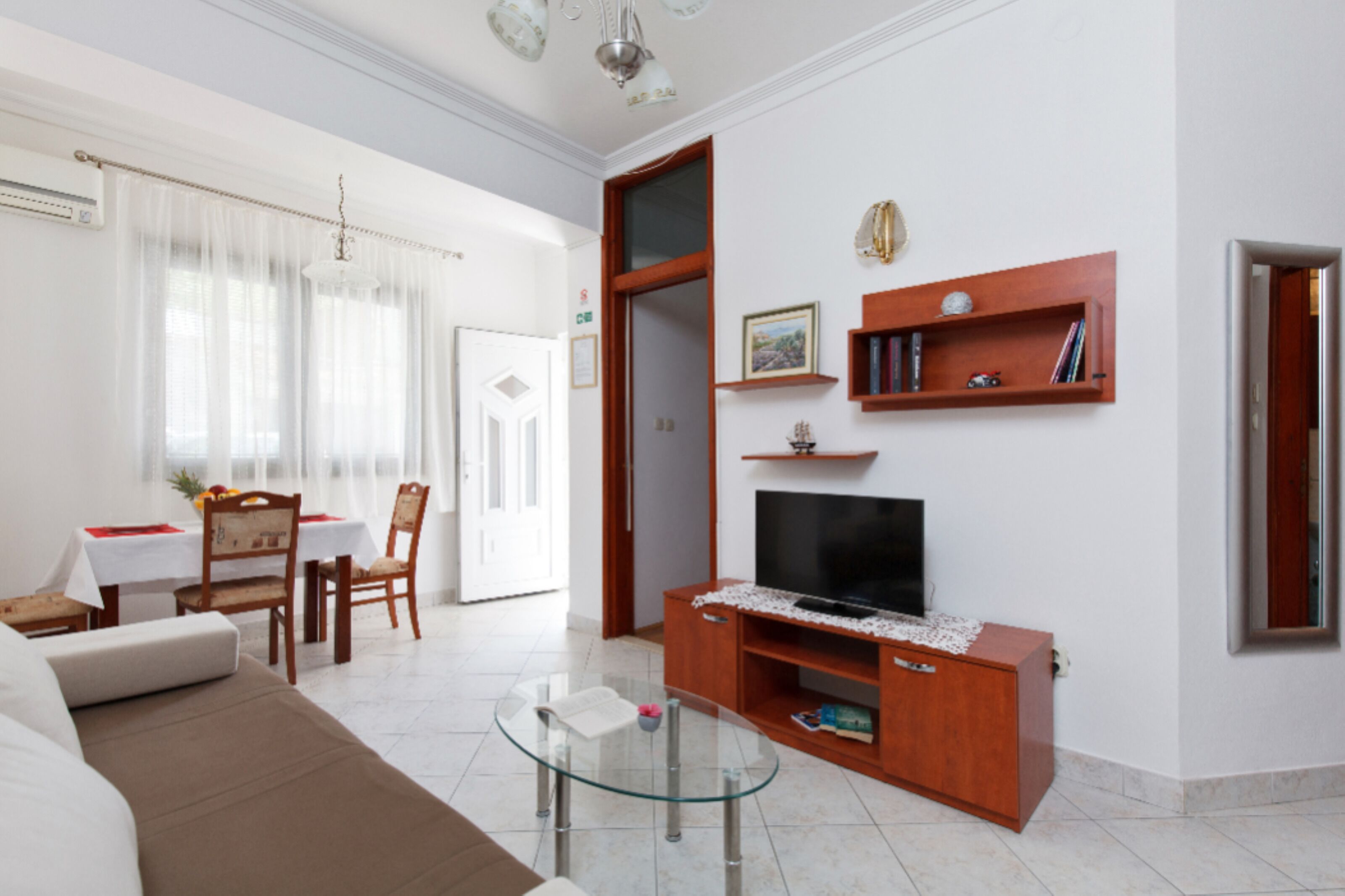 A modern living room with a sofa, glass coffee table, wooden entertainment unit, and a flat-screen TV.