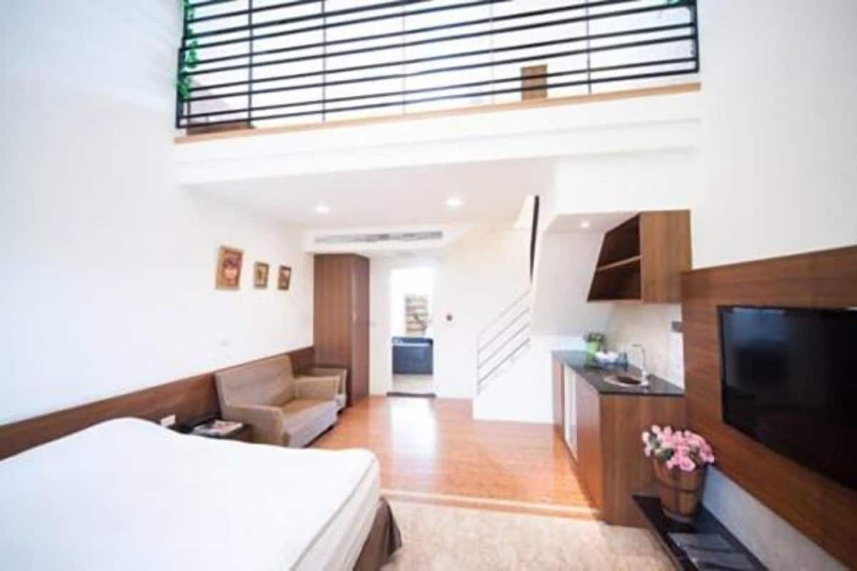 A modern hotel room with a large bed, a sofa, a TV mounted on the wall, and a balcony with a railing.