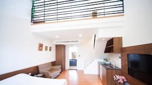 Una habitación de hotel moderna con una cama grande, un sofá, un televisor montado en la pared y un balcón con barandilla.