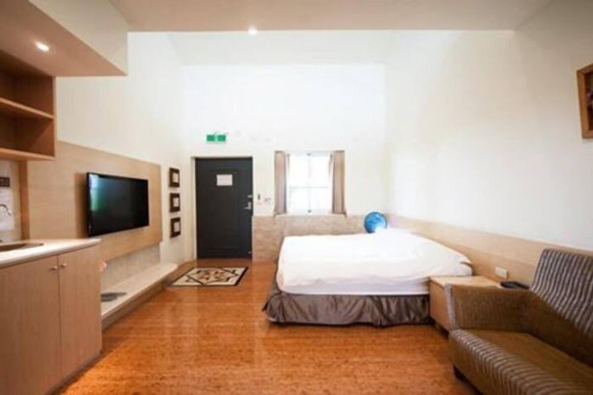 A hotel room with a bed, a television, a sofa, and a small kitchenette.