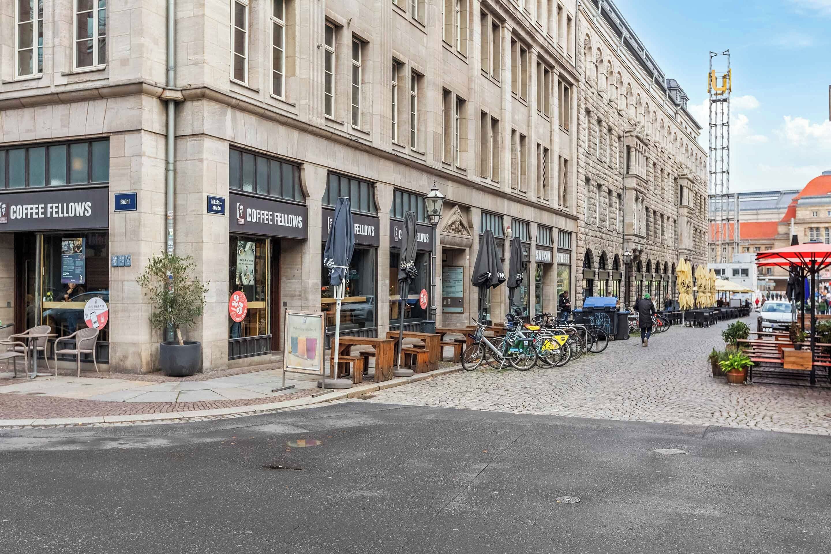 A street with a building housing 'Coffee Fellows' cafes, outdoor seating, and bicycles parked outside.