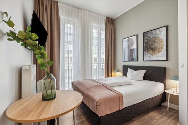 Una habitación de hotel moderna con una cama grande, una mesita de noche, un televisor montado en la pared y dos obras de arte enmarcadas.