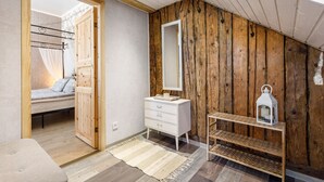 Ein Schlafzimmer mit einer Wand aus Holzlamellen, einer weißen Kommode, einem Spiegel, einem Nachttisch mit einer Laterne und einem Bett mit Baldachin.