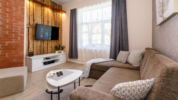 Ein modernes Wohnzimmer mit Backsteinwand, Holzvertäfelung, einem Flachbildfernseher, einer weißen Unterhaltungseinheit, einem braunen Sofa, einem weißen Couchtisch und einem großen Fenster mit Vorhängen.