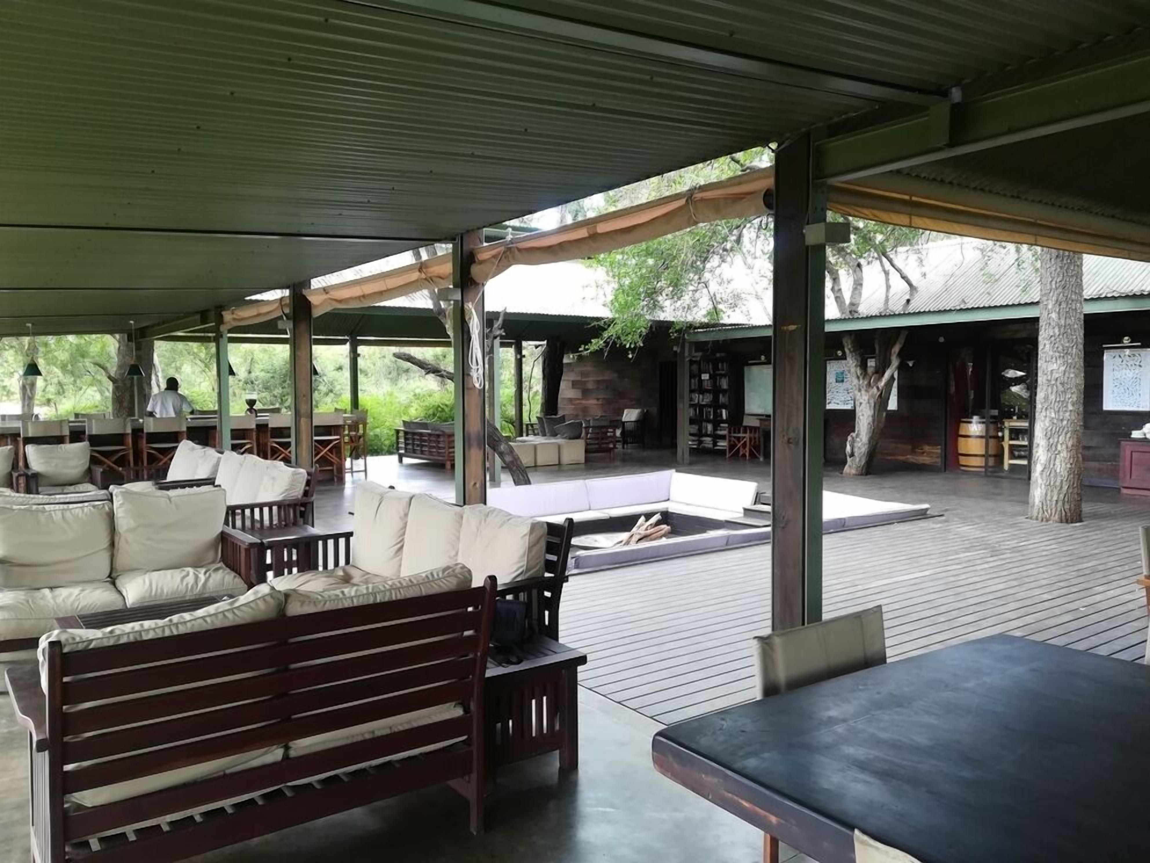 Un espace extérieur aménagé, abrité et doté de mobilier en bois et d’une cheminée en pierre.