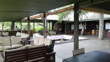 Un espace extérieur aménagé, abrité et doté de mobilier en bois et d’une cheminée en pierre.