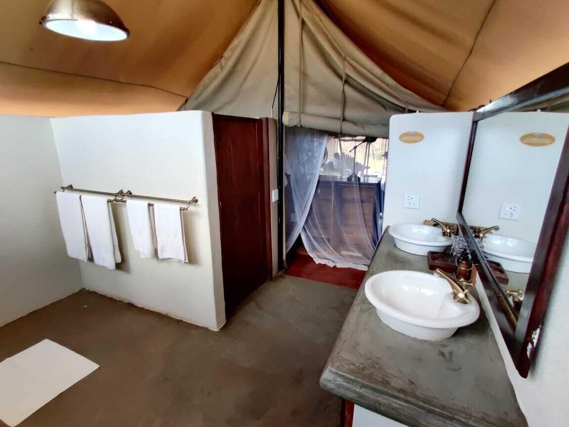 A tented room with a bathroom featuring two sinks, a mirror, and a towel rack.