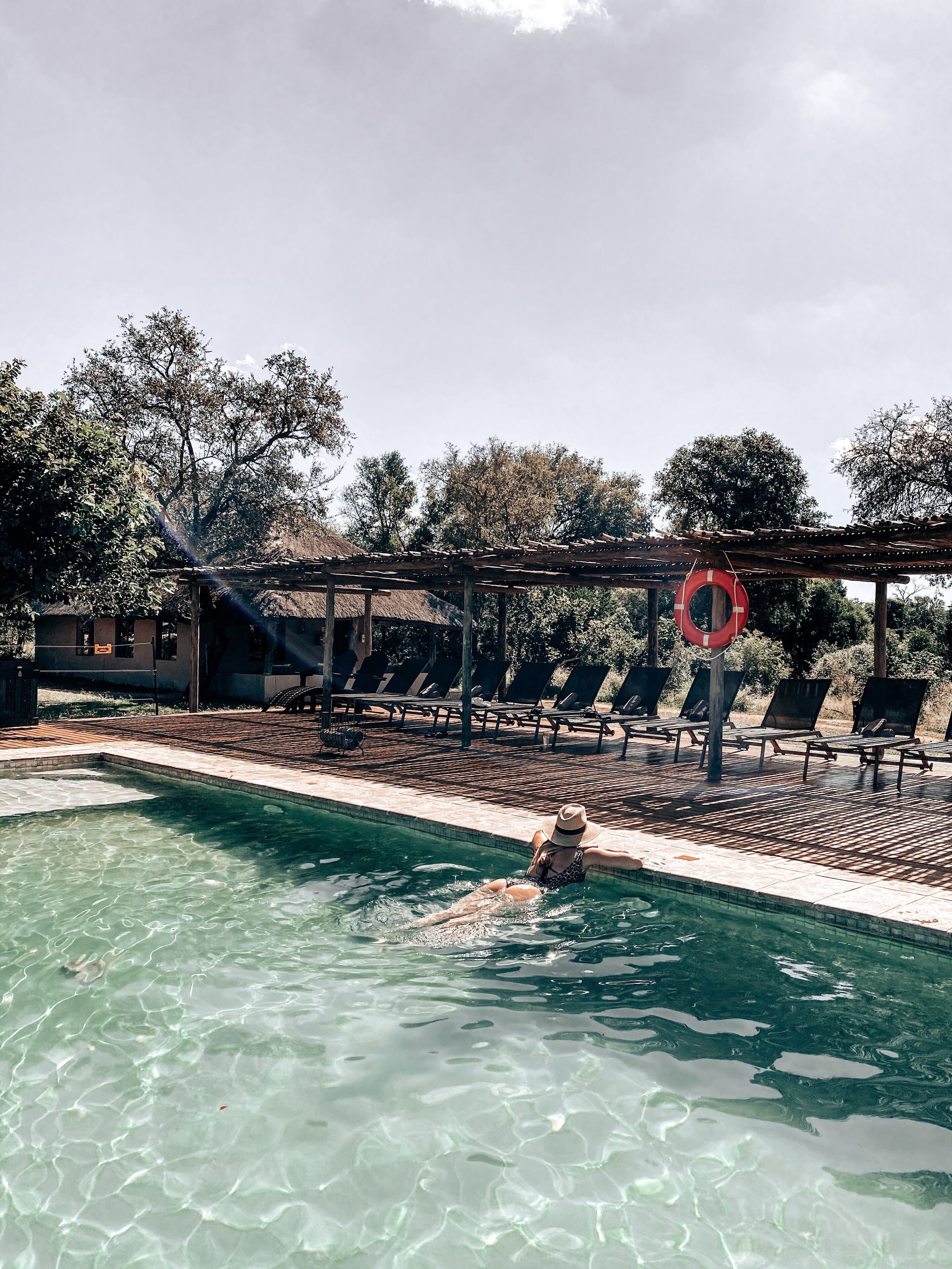 Een zwembad met helder water, omringd door ligbedden en een pergola.