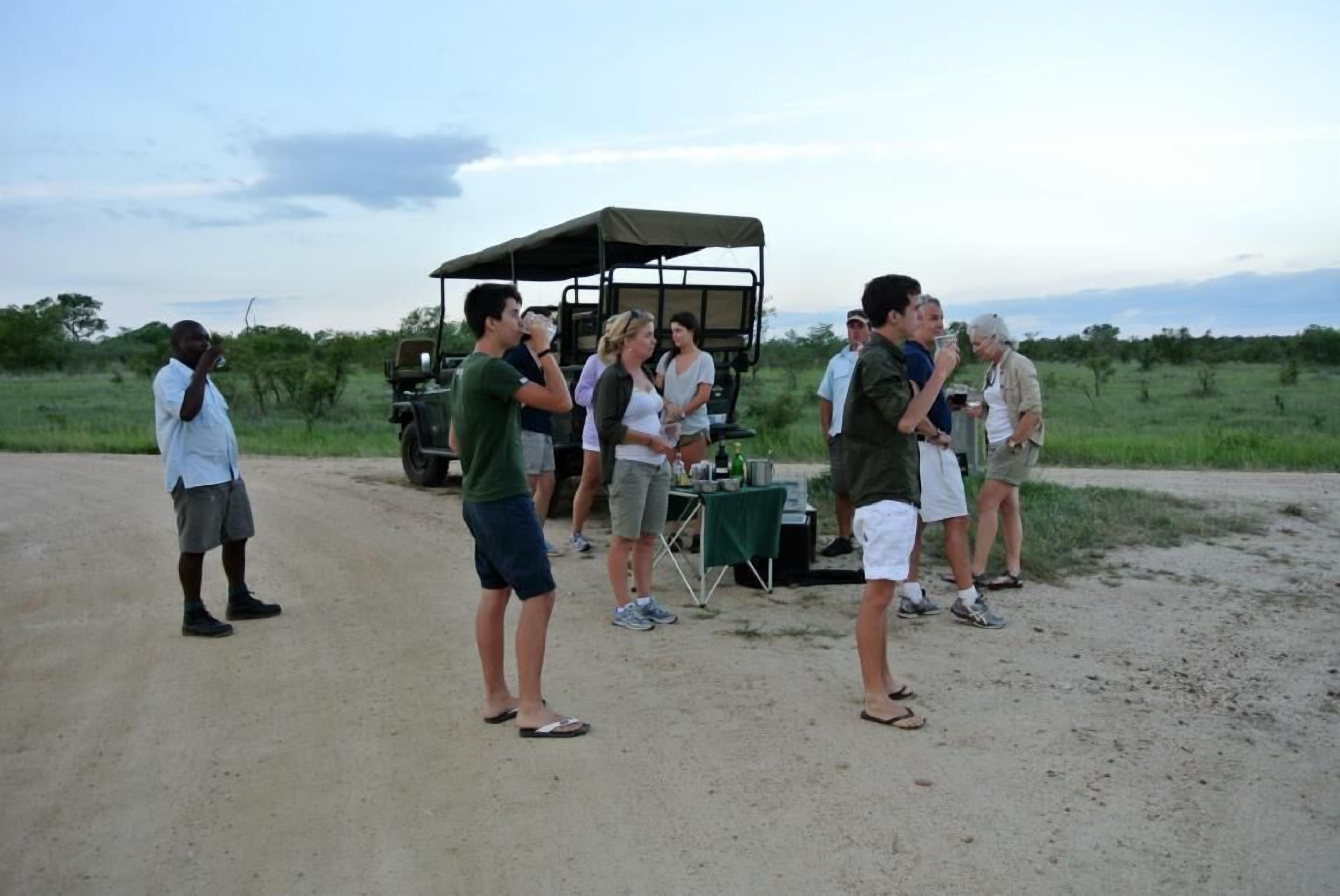Un groupe de personnes se tient sur un chemin de terre, avec un véhicule de safari en arrière-plan.