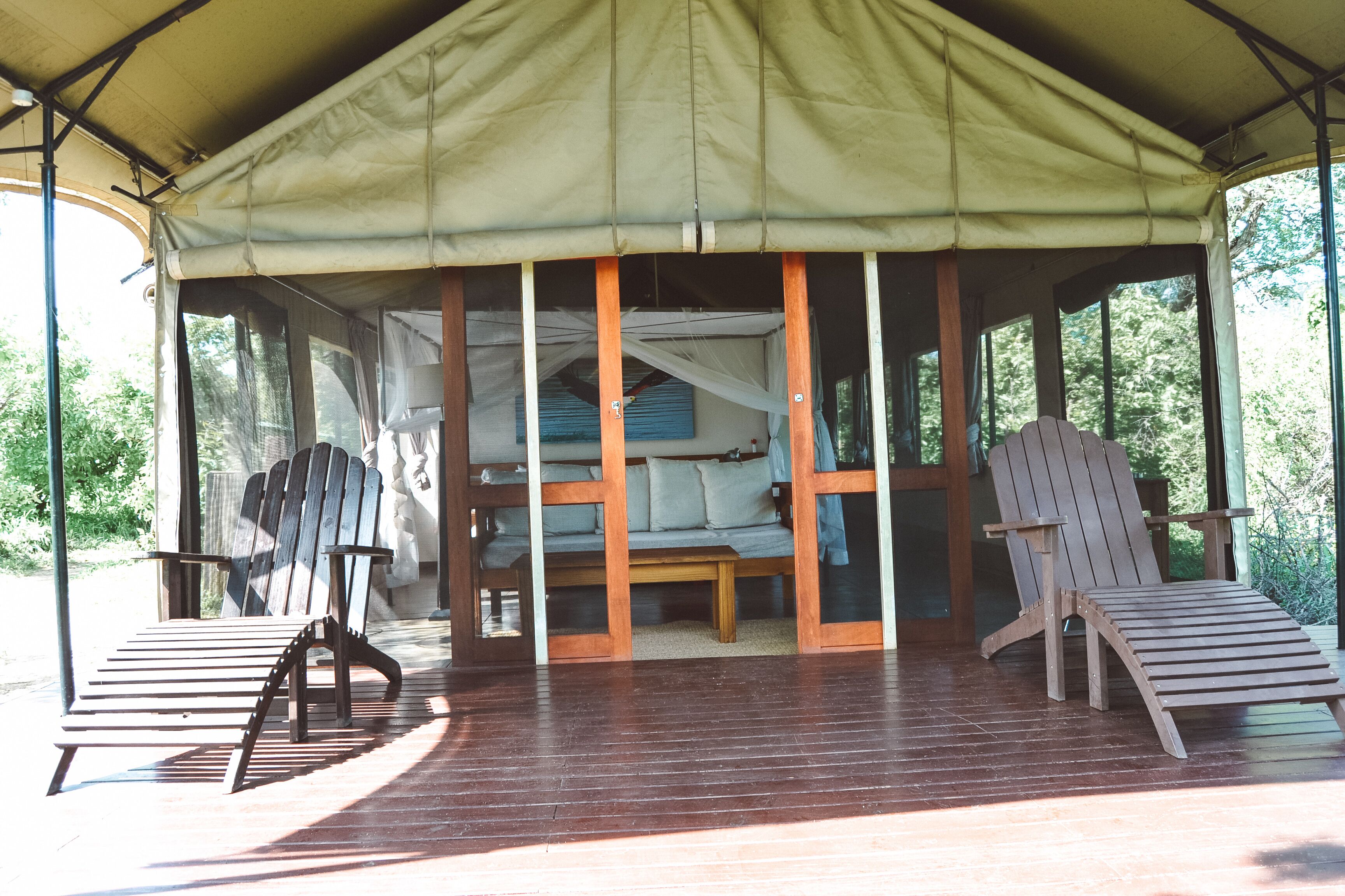 Een overdekt buitengebied met houten stoelen en een bank, onder een grote tentachtige constructie.