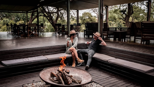 Un área de estar al aire libre con techo, una chimenea, bancos de madera y mesas.