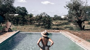 Una persona de pie en una piscina cristalina con borde de azulejos, rodeada de árboles y cielo despejado.