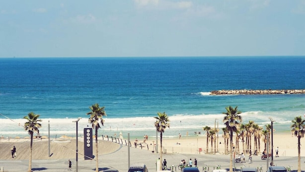 A beach with palm trees, a boardwalk, and a rocky breakwater. - Tranquil Garden Retreat by Sea N Rent (Tel Aviv)