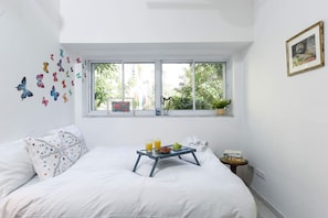 Ein Schlafzimmer mit einem Bett, einem Fenster, einem kleinen Tisch mit Tablett und einer Wand mit Schmetterlingsmotiven.