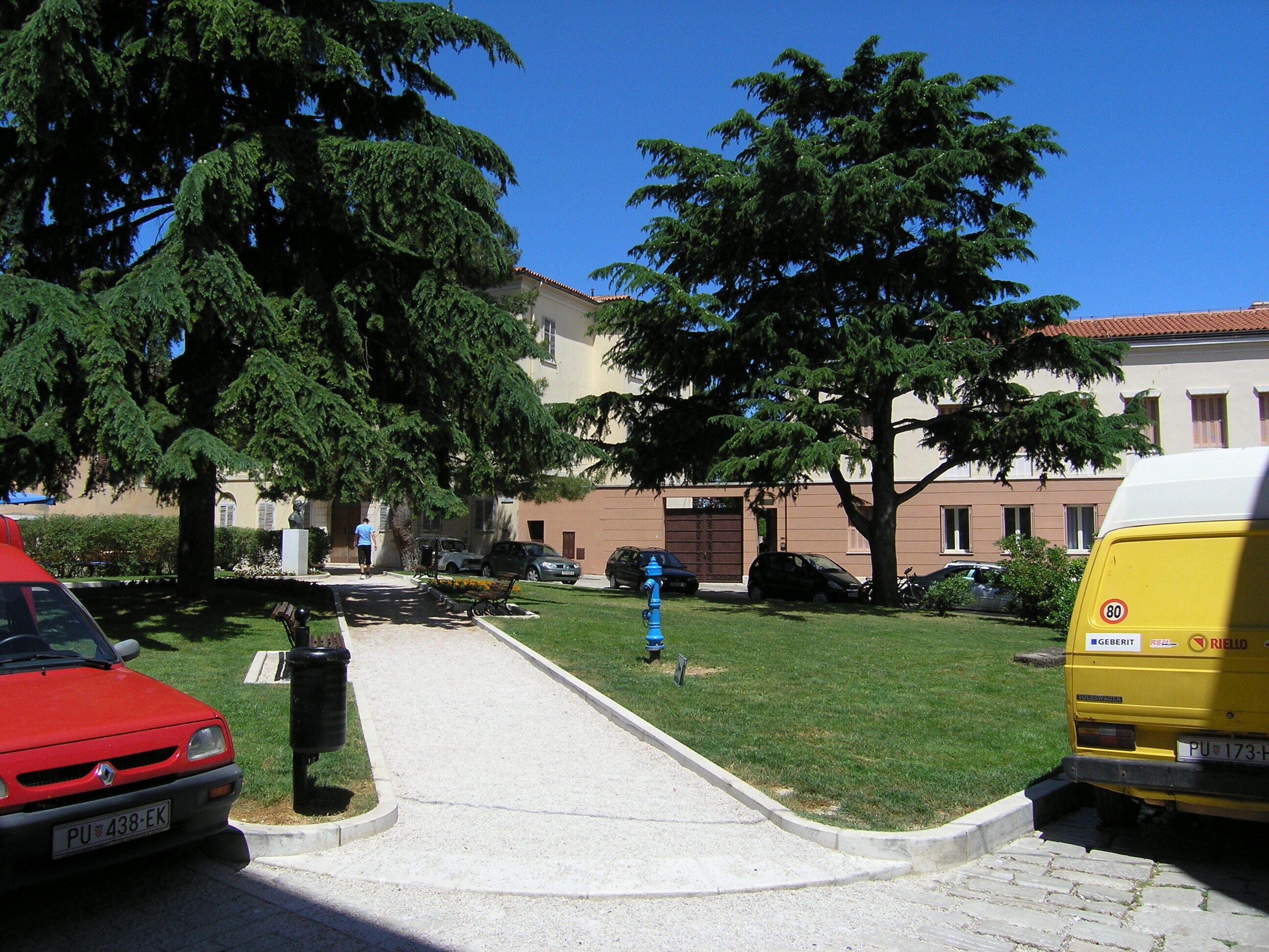 A parking area with a red car, a yellow van, and a blue fire hydrant.