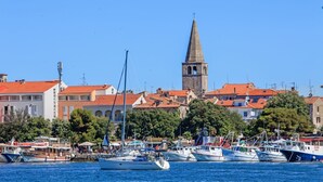 Ein Hafen mit mehreren vertäuten Booten, einem markanten Kirchturm und Gebäuden mit roten Ziegeldächern.