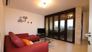 Ein Wohnzimmer mit einem roten Sofa, einem Fernseher und einer Glastür, die auf einen Balkon führt.