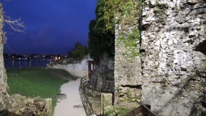 Ein Steinweg führt zu einer historischen Stätte, vorbei an einem Holzzaun und einer Mülltonne.