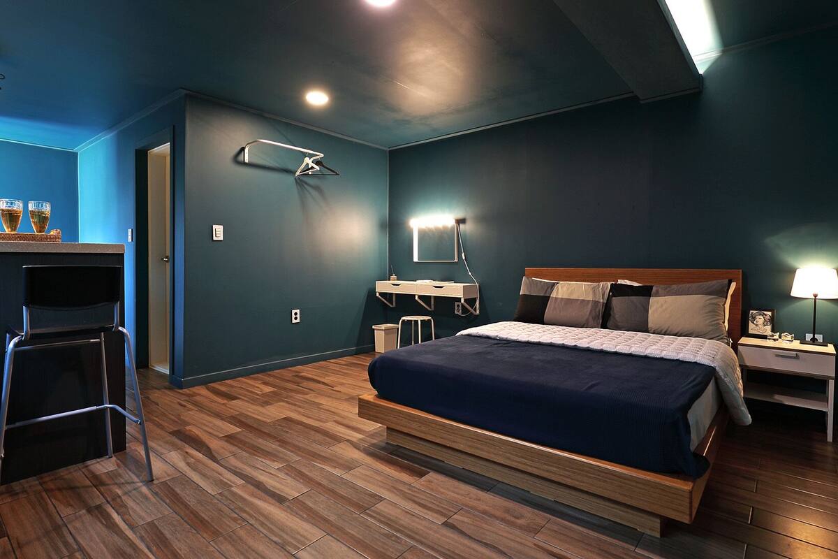 Een moderne slaapkamer met een bed, nachtkastje, lamp en bureau met stoelen.