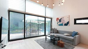 Ein modernes Wohnzimmer mit einer großen Schiebeglastür, die zu einem Außenbereich führt, ein graues Sofa, ein Couchtisch und ein Gemälde an der Wand.