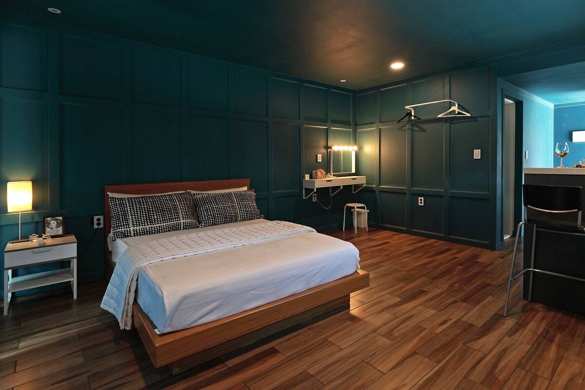 Een moderne slaapkamer met een houten bed, een nachtkastje, een spiegel en een klein krukje.