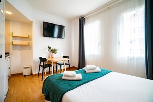 Camera d'albergo con un letto, una scrivania, sedie, una TV e una finestra con tende.