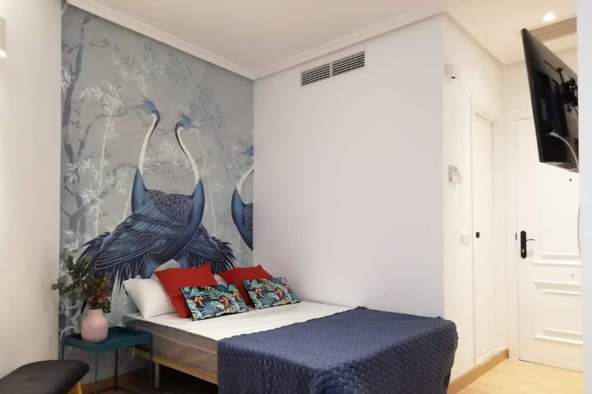 Ein Schlafzimmer mit Bett, Schreibtisch und Wandgemälde von Vögeln.