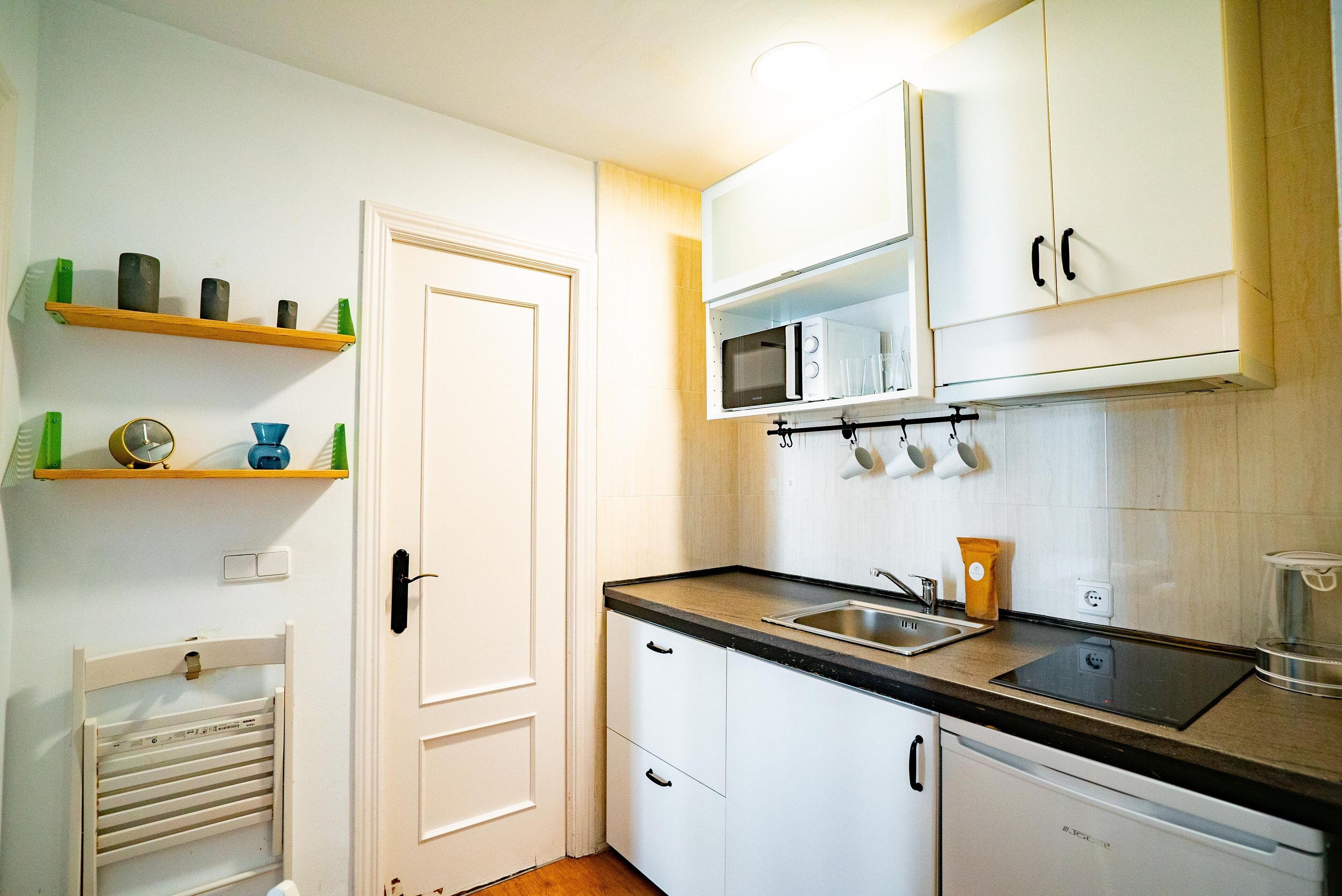 Une cuisine compacte avec des meubles blancs, un plan de travail noir, un four à micro-ondes et un four encastré.