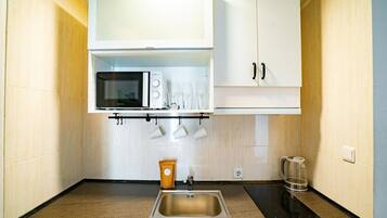 Una cocina compacta con un lavamanos de acero inoxidable, un microondas y una cafetera.