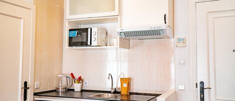 Una cocina compacta con microondas, cafetera y un lavamanos pequeño.