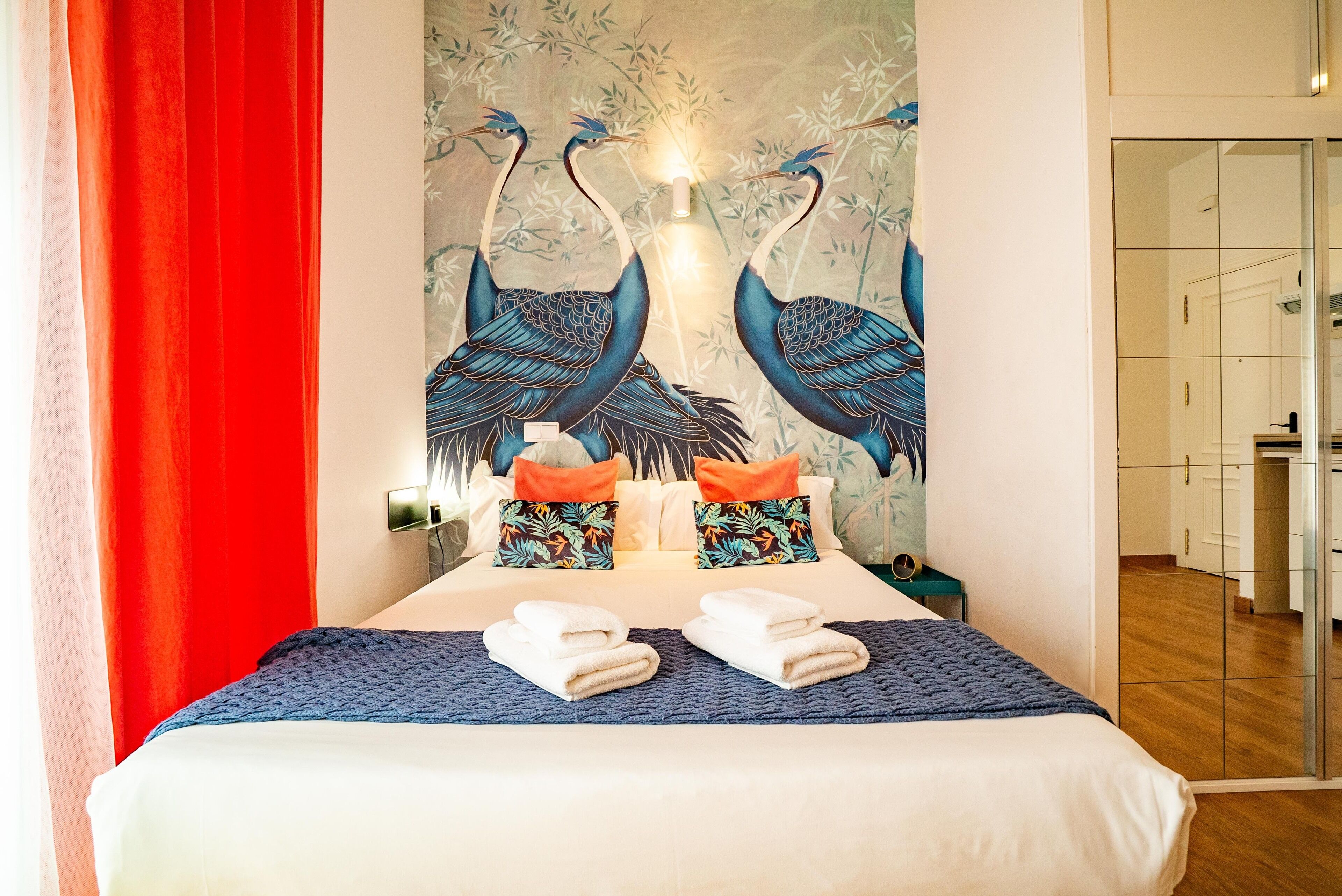 A hotel room with a bed, pillows, towels, and a wall mural of birds.