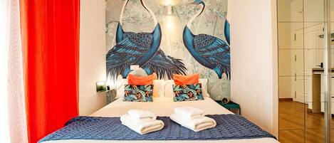 A hotel room with a bed, pillows, towels, and a wall mural of birds.