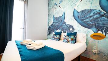 A hotel room with a bed, towels, and a mural of birds on the wall.
