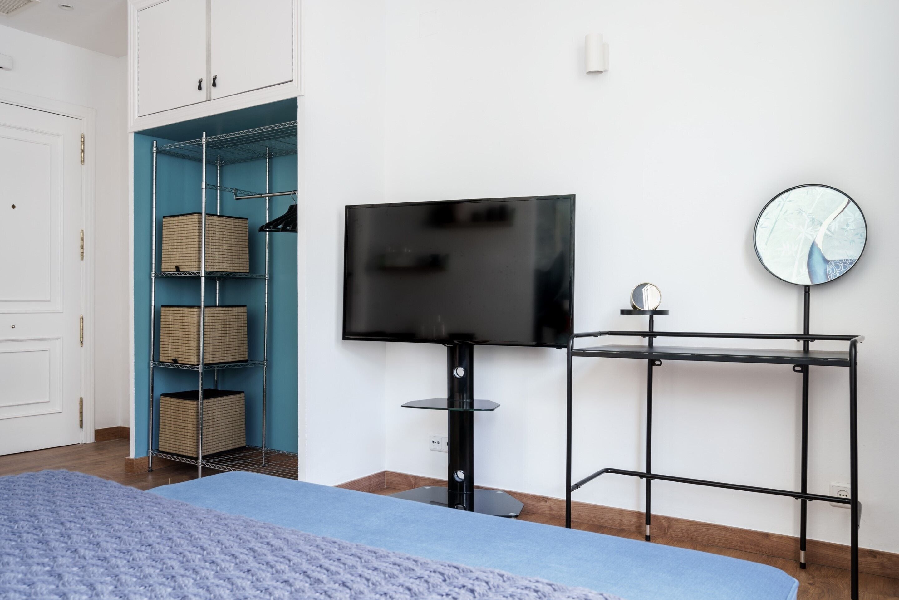 A bedroom with a bed, a TV on a stand, a wardrobe, and a mirror on a small table.
