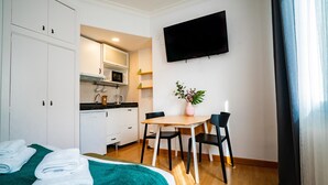 A compact hotel room with a bed, a small kitchenette, a dining table with chairs, and a TV mounted on the wall. - Smartr Madrid Gran Vía 47 (Madrid)
