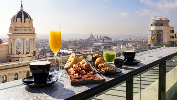 A rooftop terrace with a city view, a glass of orange juice, a cup of coffee, and a variety of pastries and meats. - Smartr Madrid Gran Vía 47 (Madrid)