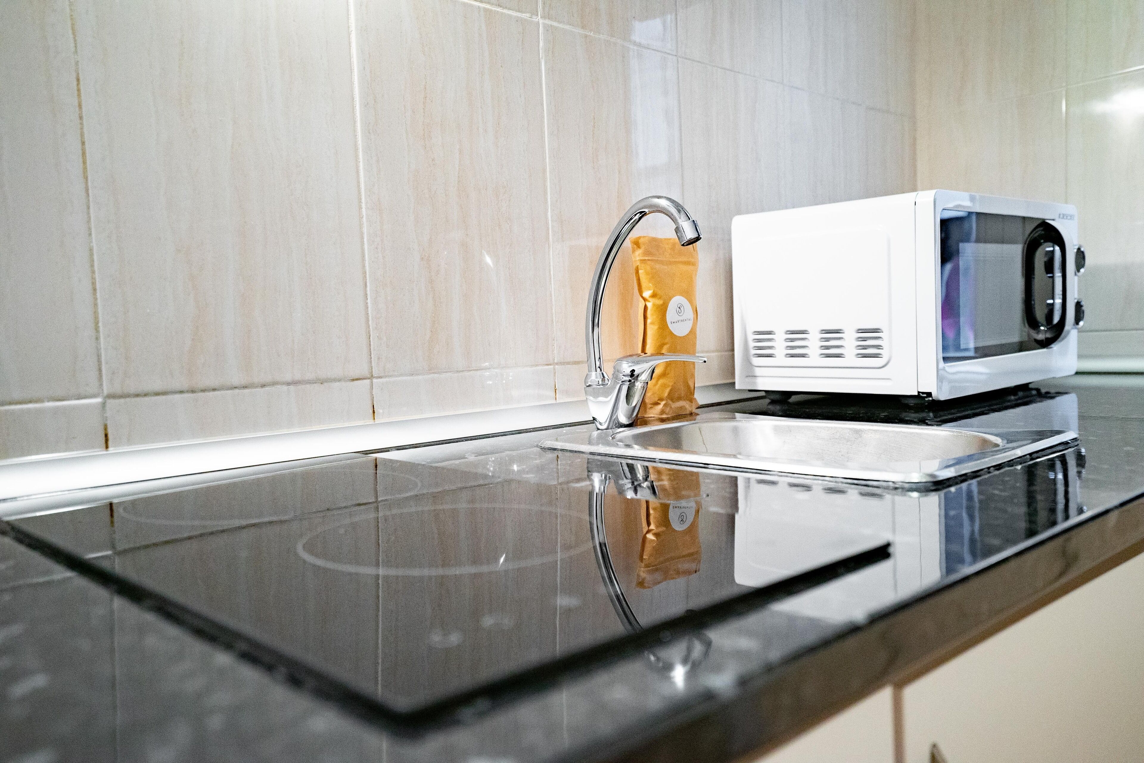 A kitchen with a stainless steel sink, a white microwave, and a paper towel dispenser.