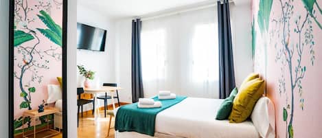 A modern hotel room with a bed, a desk, a chair, a TV, and a large mirror.