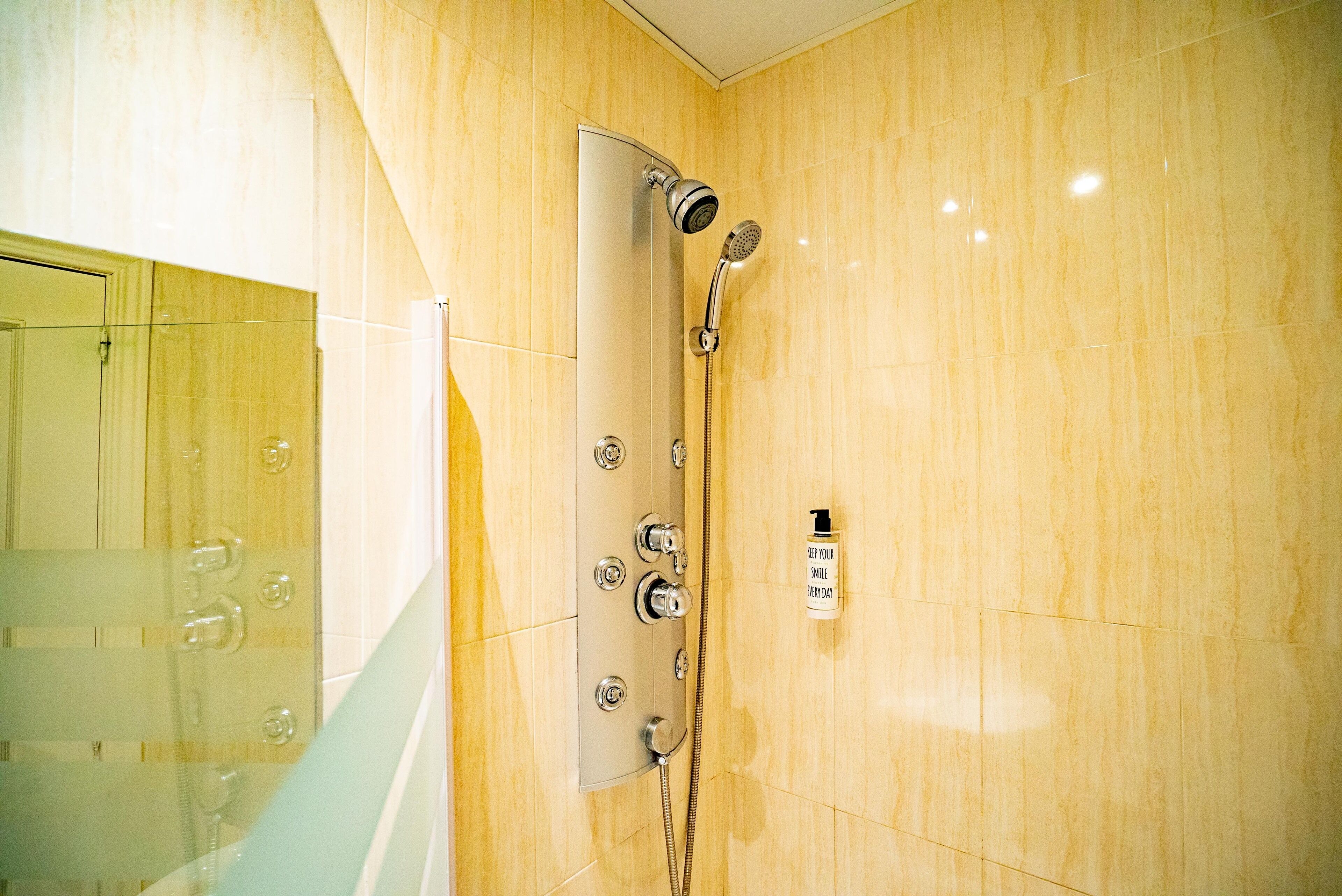 Un baño moderno con cabina de ducha de vidrio, ducha con cabezal de mano y panel de control en la pared.