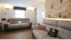 Een woonkamer met twee banken, een stenen muur met decoratieve objecten en een raam met zonwering.