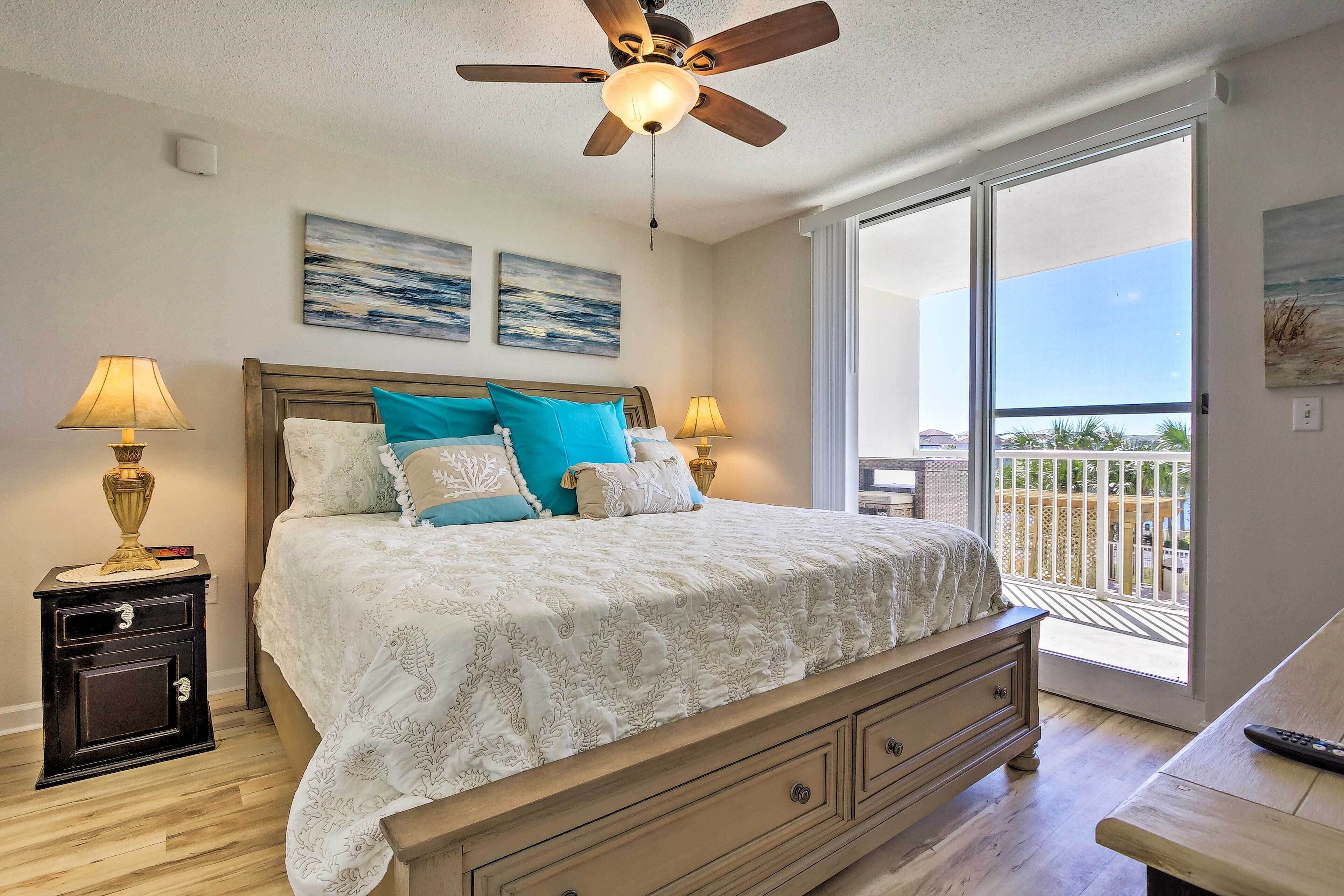 A bedroom with a bed, two nightstands, a ceiling fan, and a balcony with a view.