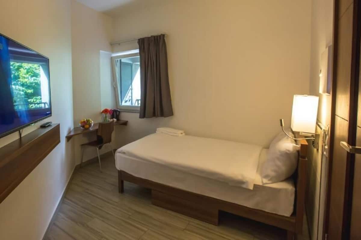Quarto de hotel com uma cama, uma mesa, uma televisão e uma janela com cortinas.